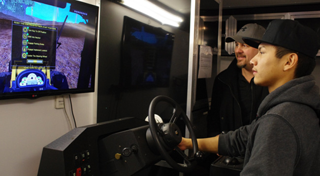Paul Giles, manager of ORIGIN - Operator Recruitment and Training, watches a student try out a heavy equipment virtual simulator during the Feb. 18 career fair at Dennis Franklin Cromarty First Nations High School in Thunder Bay.